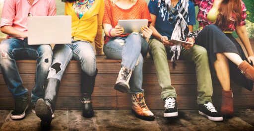 teenagers sitting on a wooden bench with laptops and tablets